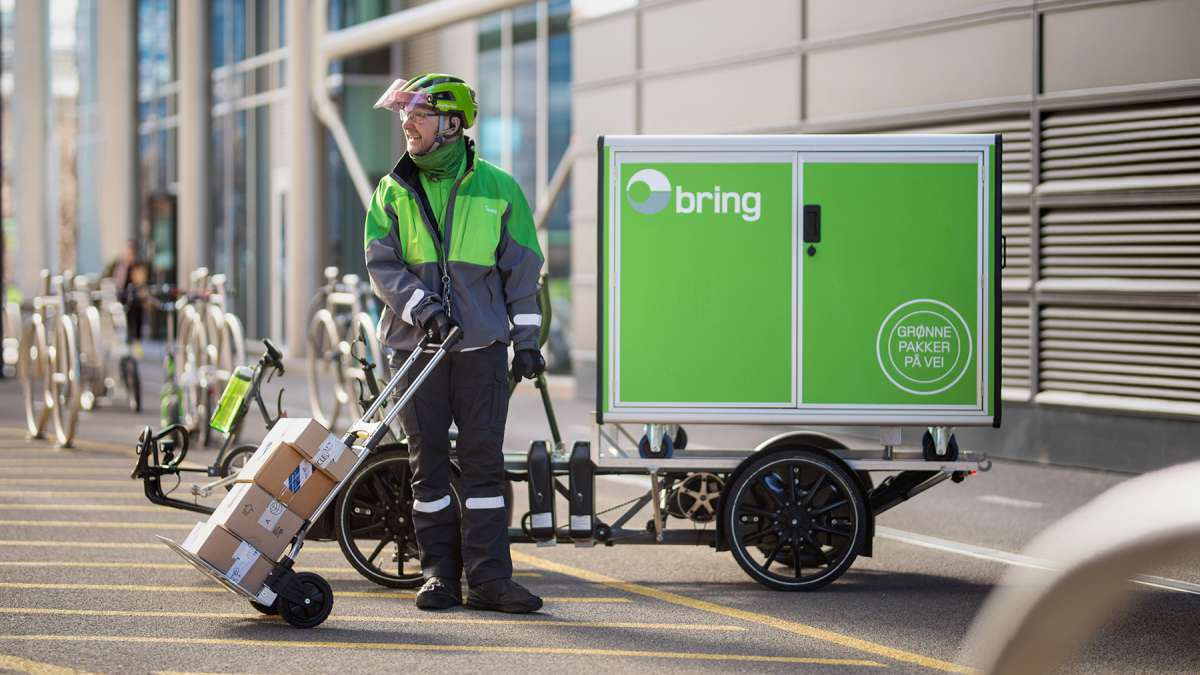 En mann i Bring-uniform som holder en sekketralle med fire pakker