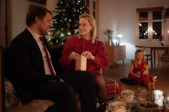 kvinne åpner julegave foran juletre, sammen med mann og barn.