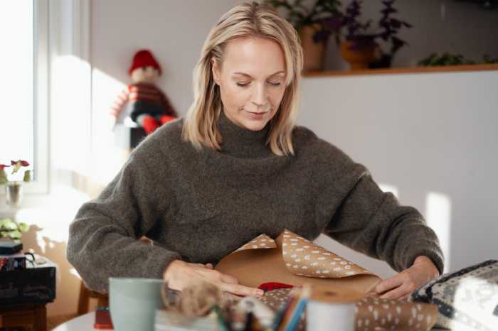 En kvinne sitter ved et bord og pakker inn en julegave.