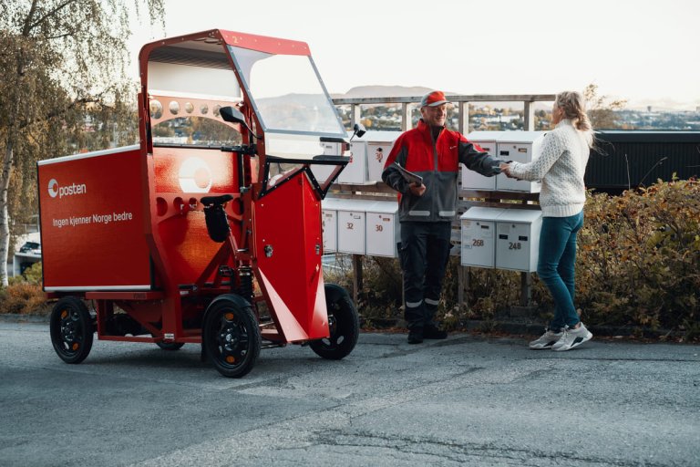 Et postbud og en dame står ved postkasser