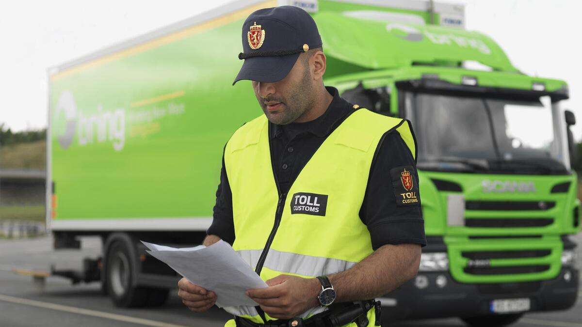 Toller sjekker tolldokumenter foran en grønn Bring lastebil.